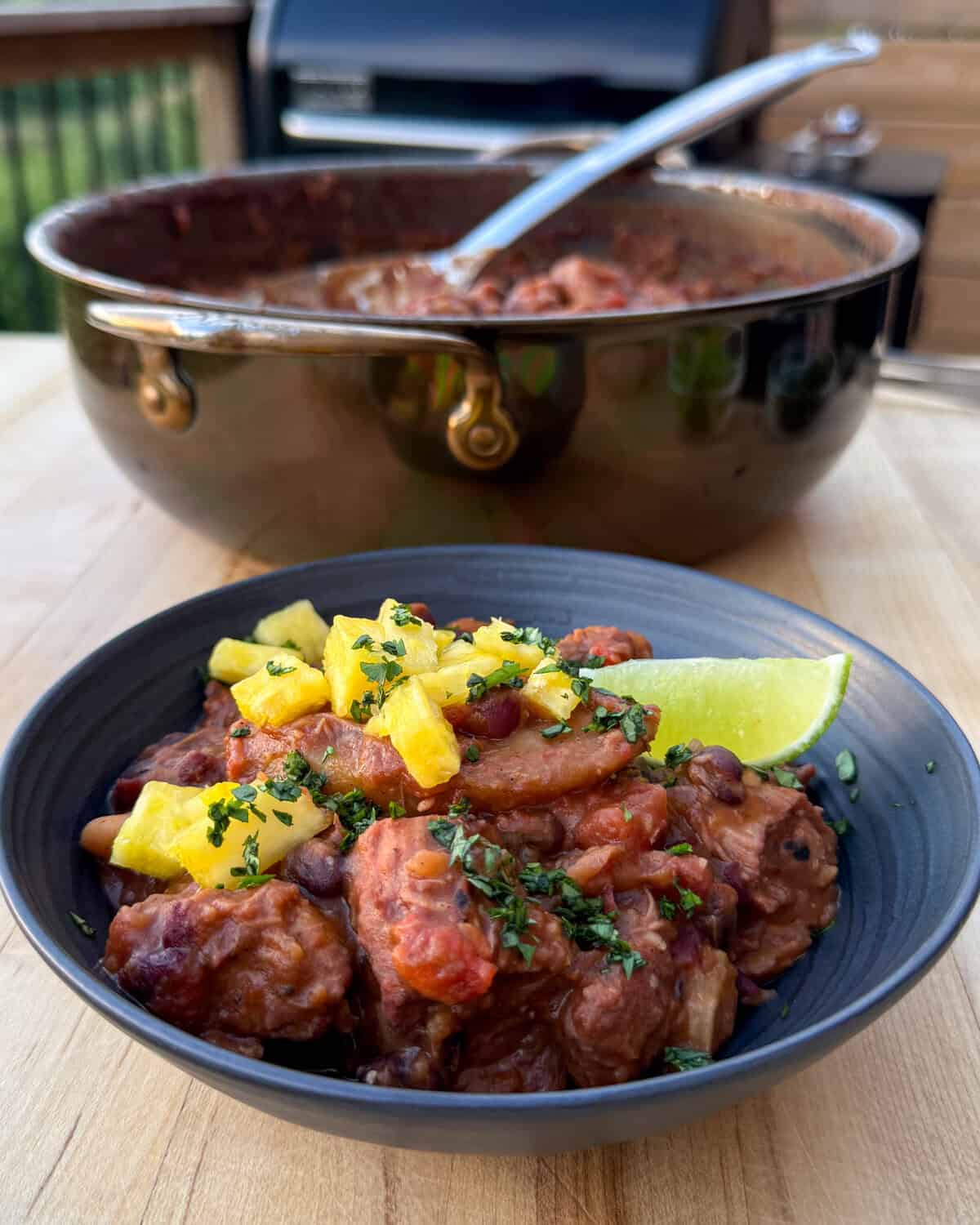 A plated bowl of Caribbean baked beans topped with pineapple, parsley and a lime wedge.
