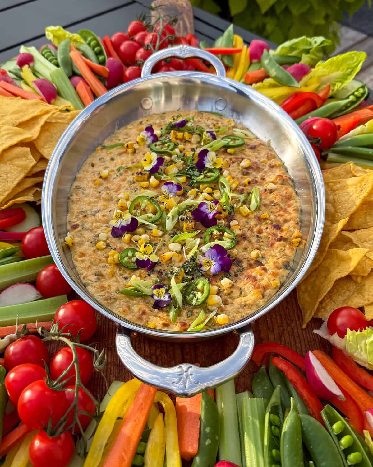 A close-up of a Charred Corn, Poblano and Jalapeño Dip served with veggies and chips.