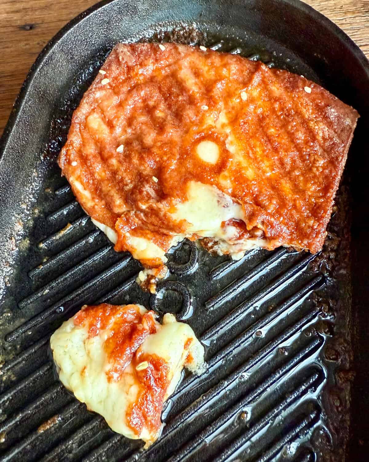 A piece of Greek fried cheese ripped open on an Ooni cast-iron skillet.