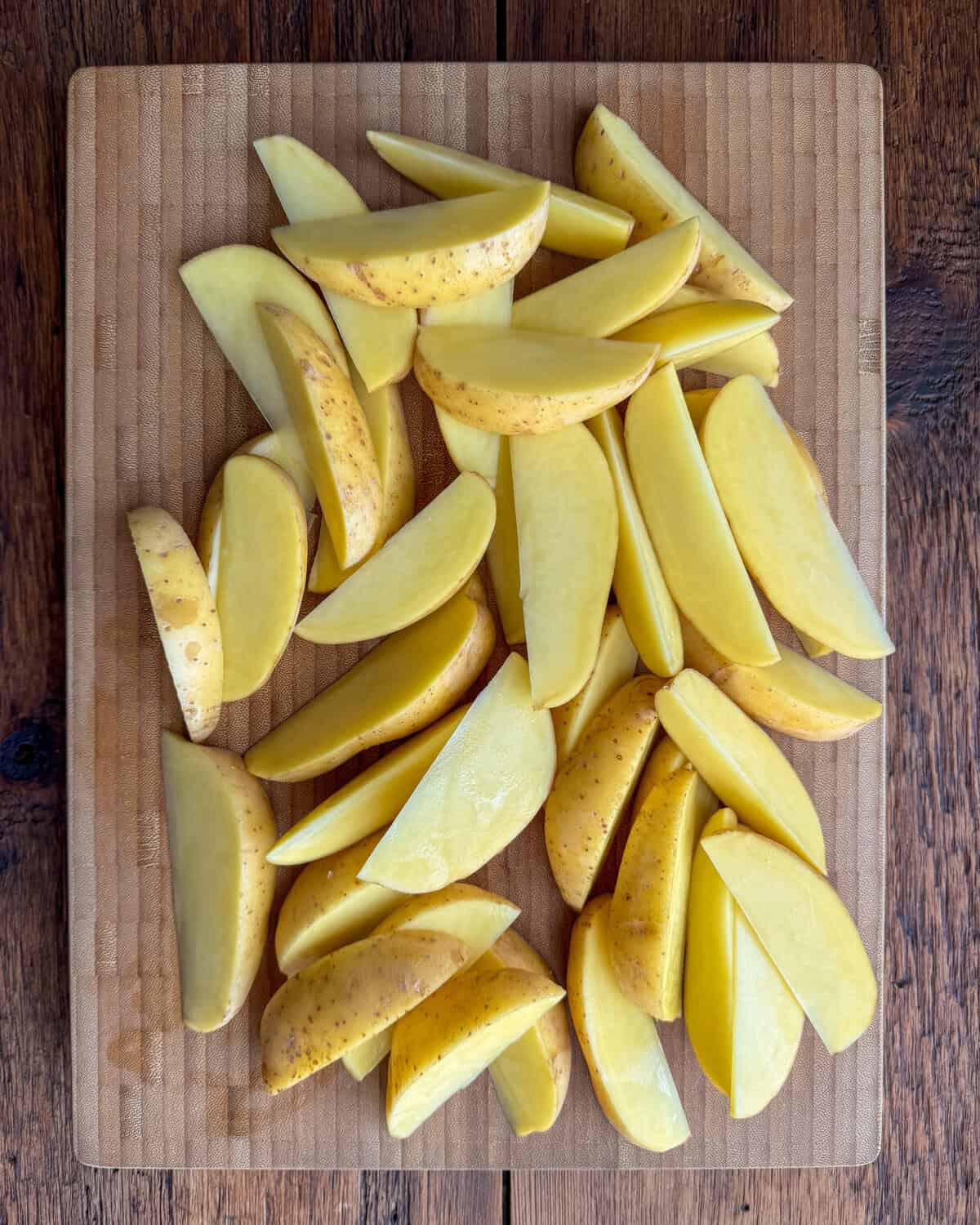 A cutting board with potato wedges for a lemon potato wedges recipe.