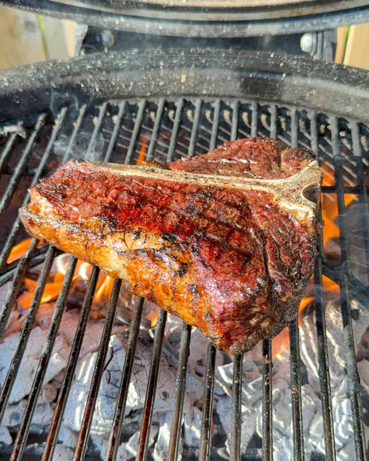 A steak getting seared over a flaming grill with grill marks.