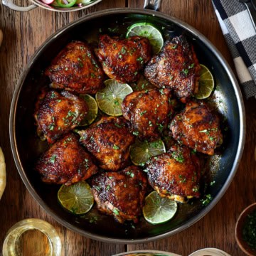 A skillet with sticky chicken thighs and lime slices.