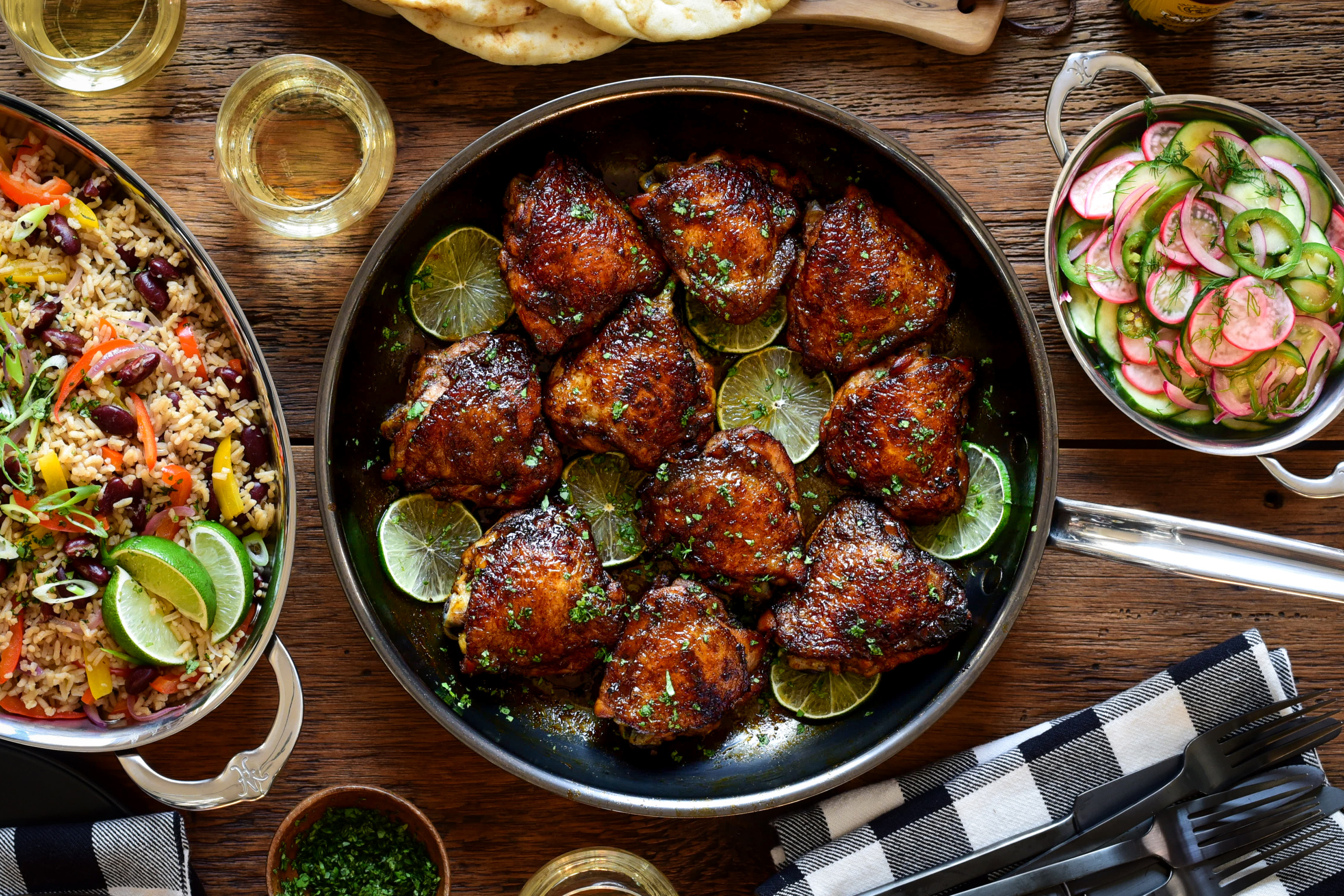 A skillet of sticky rum glazed chicken thighs served with a cucumber and radish salad and rice with beans and peppers.