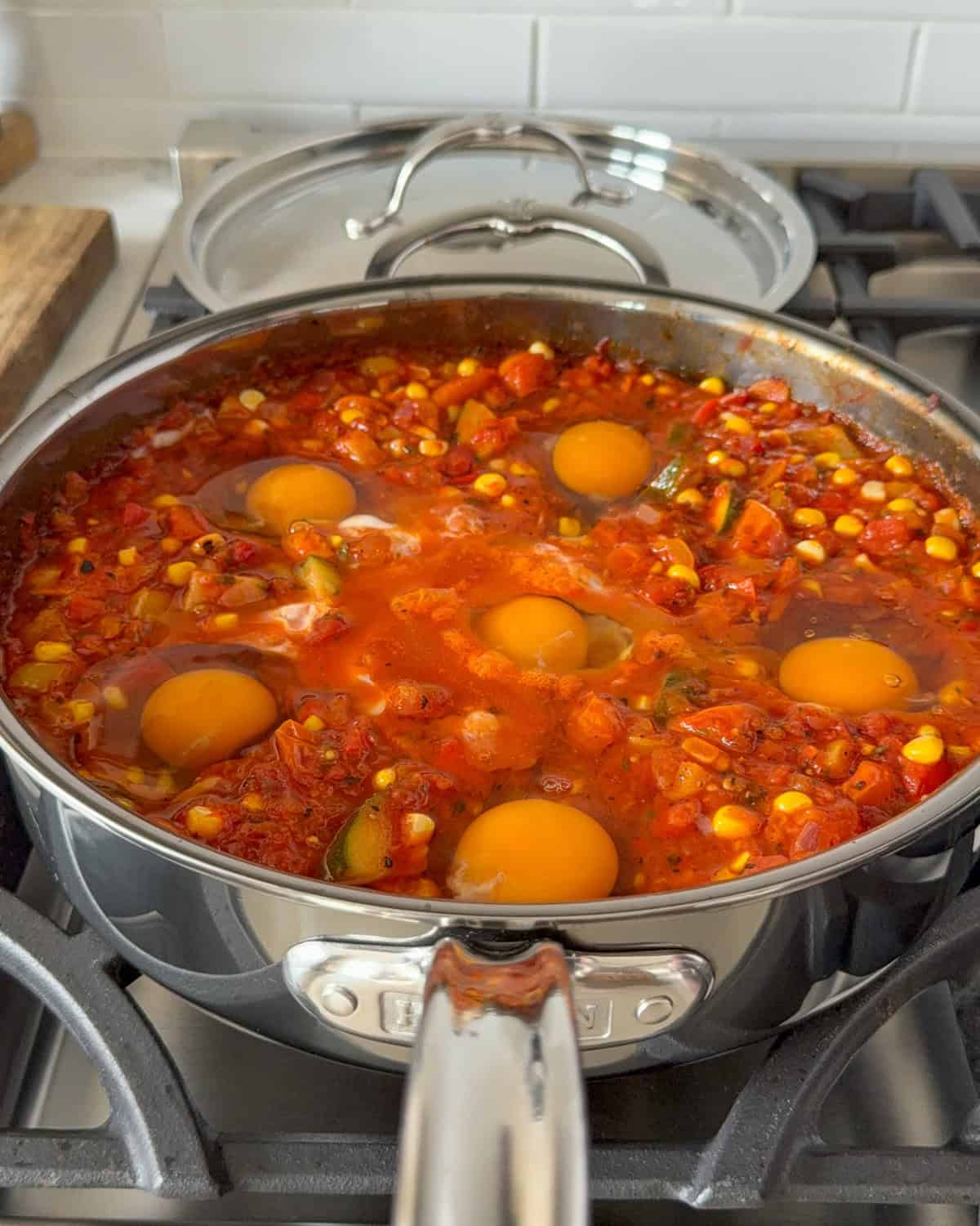 A summer vegetable shakshuka with six eggs nestled into the sauce and ready to go in the oven.
