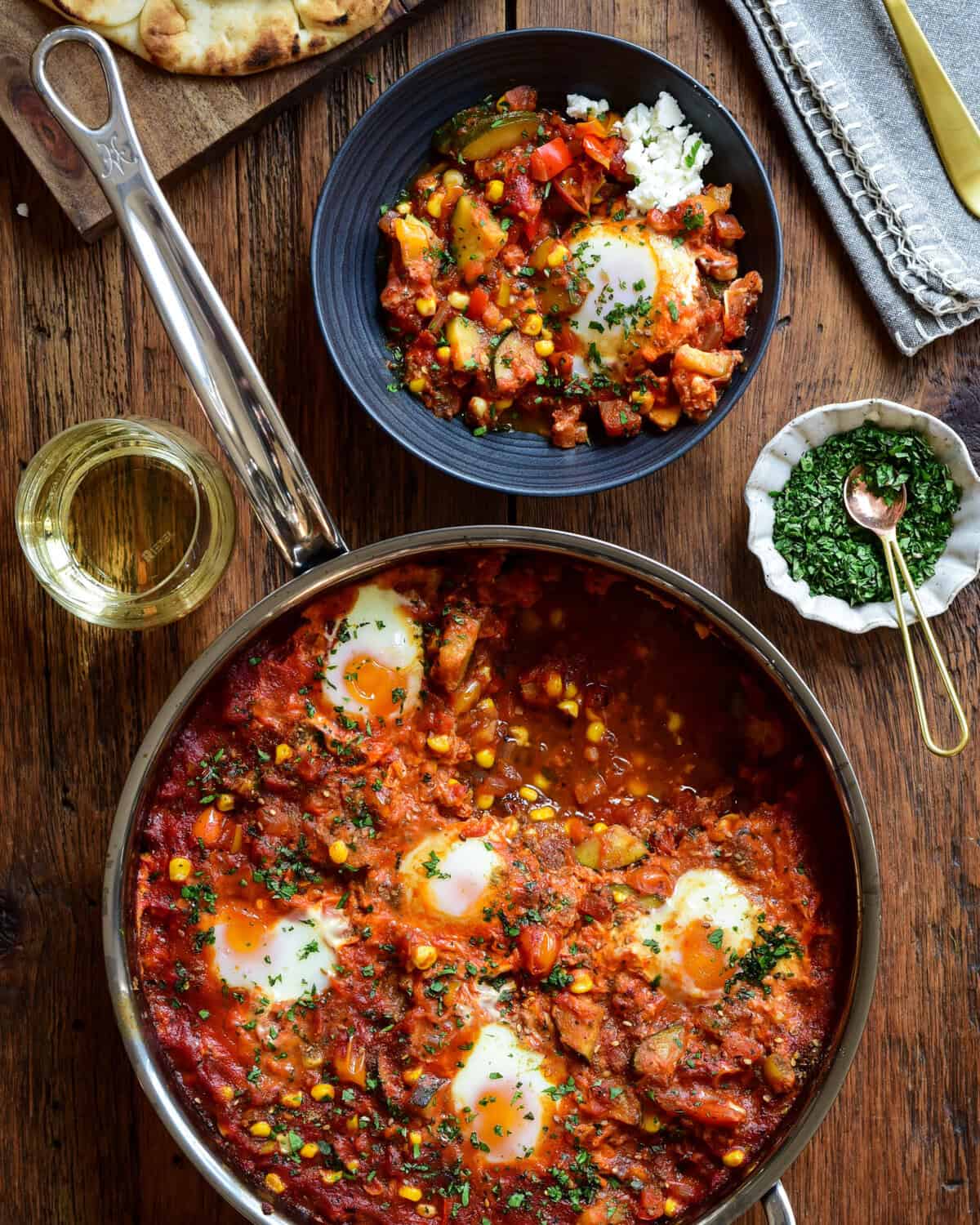 A summer vegetable shakshuka in a pan with a portion served in a bowl.