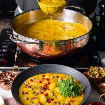 A copper pot filled with a squash soup with gnocchi and spinach.