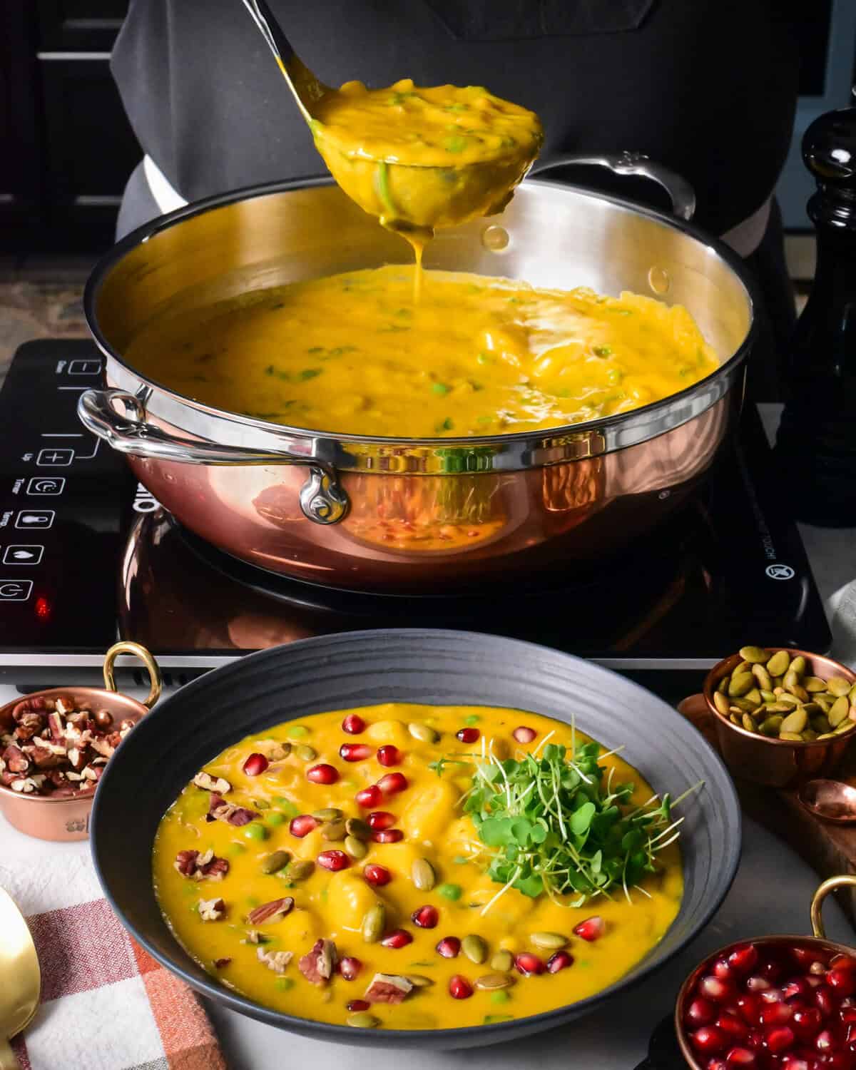 A copper pot filled with a squash soup with gnocchi and spinach.