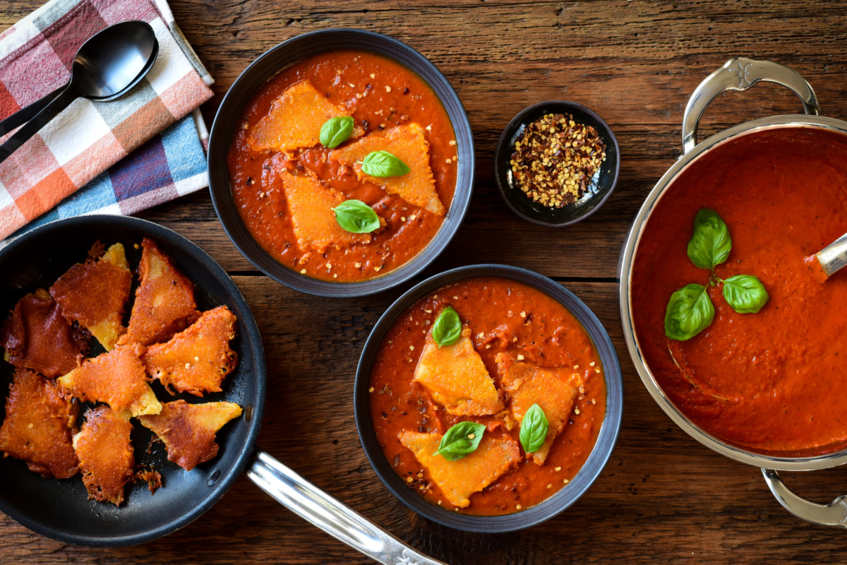 A pot and two bowls of roasted red pepper tomato soup served with grilled cheese dumplings.