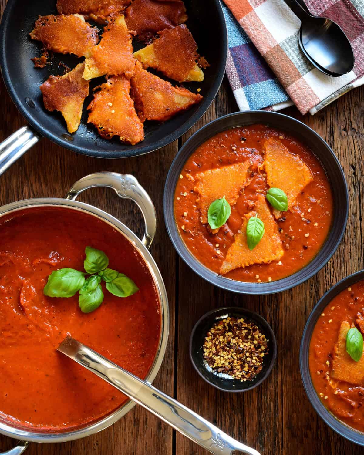 A pot of roasted red pepper tomato soup. Two bowls of soup served with three inside-out grilled cheese dumplings and fresh basil.