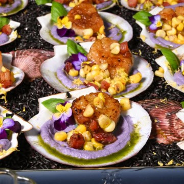 A tray filled with seared scallops with cauliflower puree and pancetta.