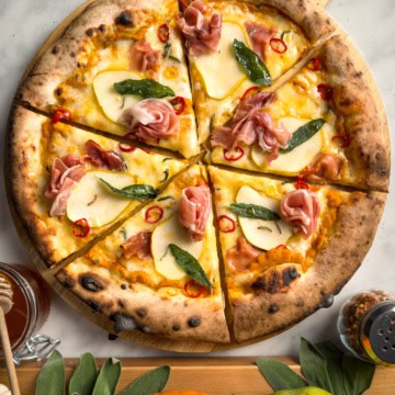 A pumpkin pear pizza with prosciutto, sage, chilis and hot honey sliced into six pieces.