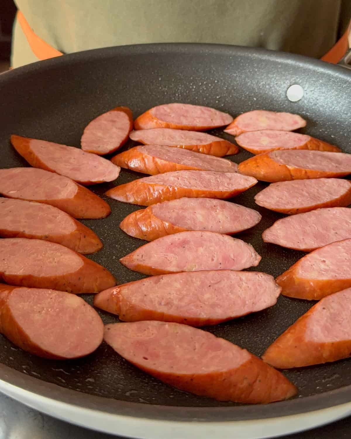 Place the kolbassa slices into the pan to fry.