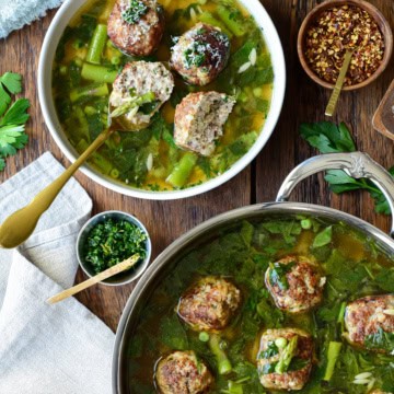 A serving and a pot of chicken ricotta meatballs with lemon orzo brodo, served with grated Parmesan, chili pepper, and a lemon-herb gremolata.