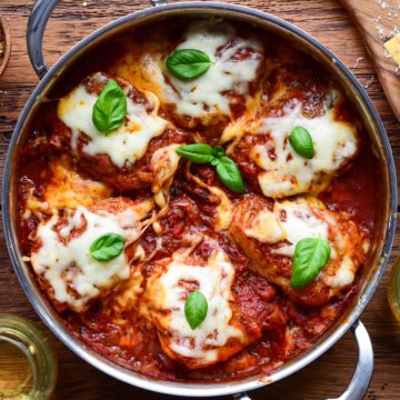 Tomato braised chicken parm thighs topped with melted cheese and fresh basil.