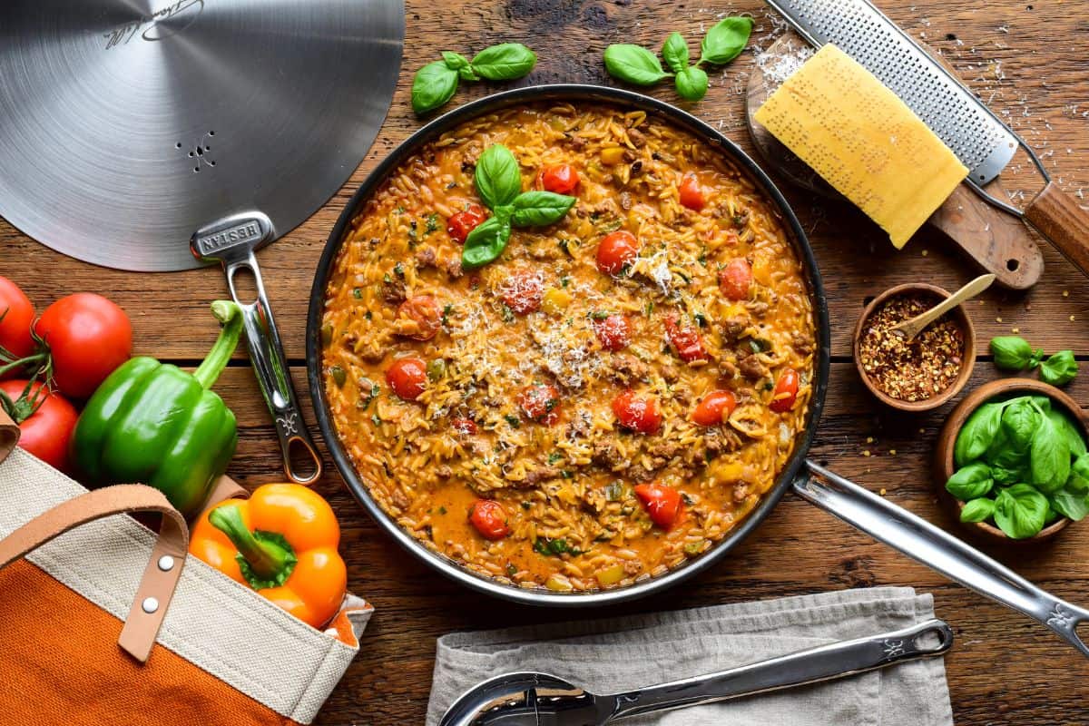 A creamy sausage, pepper & tomato orzo skillet served with shaved Parmesan and fresh basil.