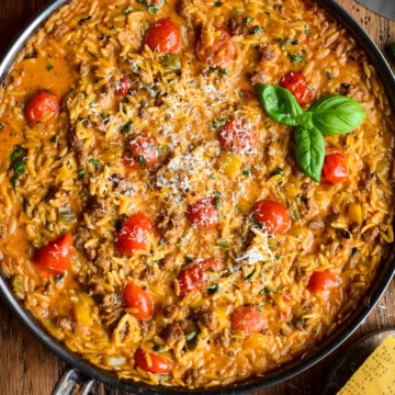 A creamy sausage, pepper & tomato orzo skillet topped with shaved Parmesan and fresh basil.