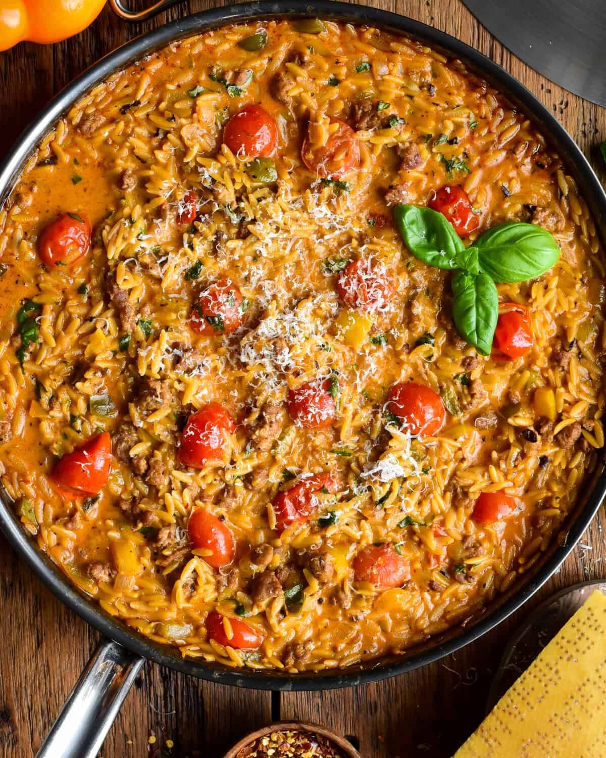 A creamy sausage, pepper & tomato orzo skillet topped with shaved Parmesan and fresh basil.