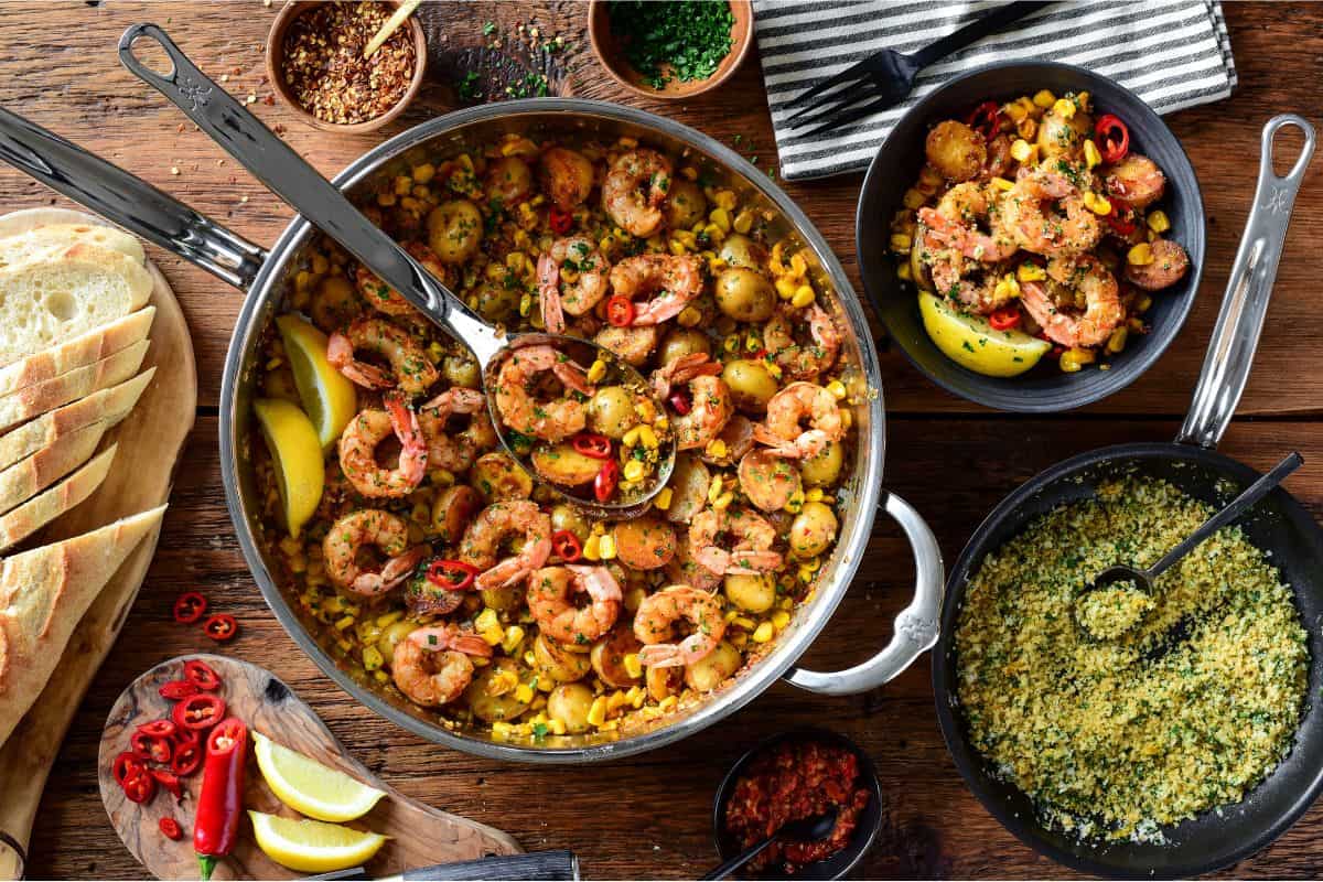 A skillet of spicy Calabrian shrimp with corn and potatoes. Served in a bowl with a lemon pangrattato sprinkled over it and extra toppings on the side.