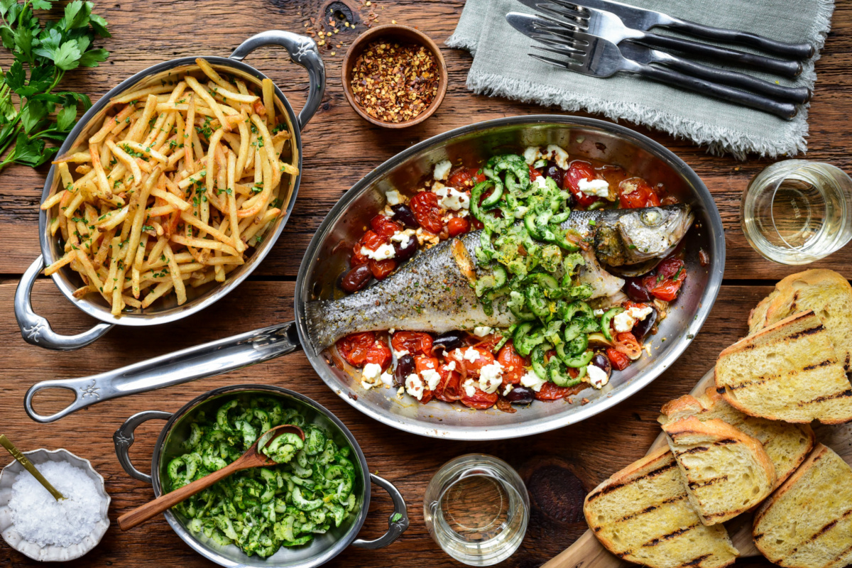 A Greek Style Whole Roasted Branzino with Tomatoes & Feta served with shoestring fries, toasted sourdough bread and topped with a cucumber herb salad.