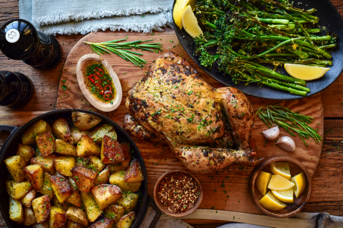 A whole rotisserie chicken served with golden duch fat potatoes and charred broccolini.