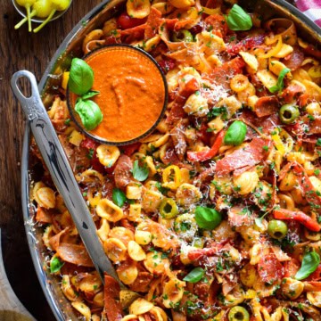 A chopped Italian romesco pasta salad with crispy spicy deli meats in a platter with extra sauce.