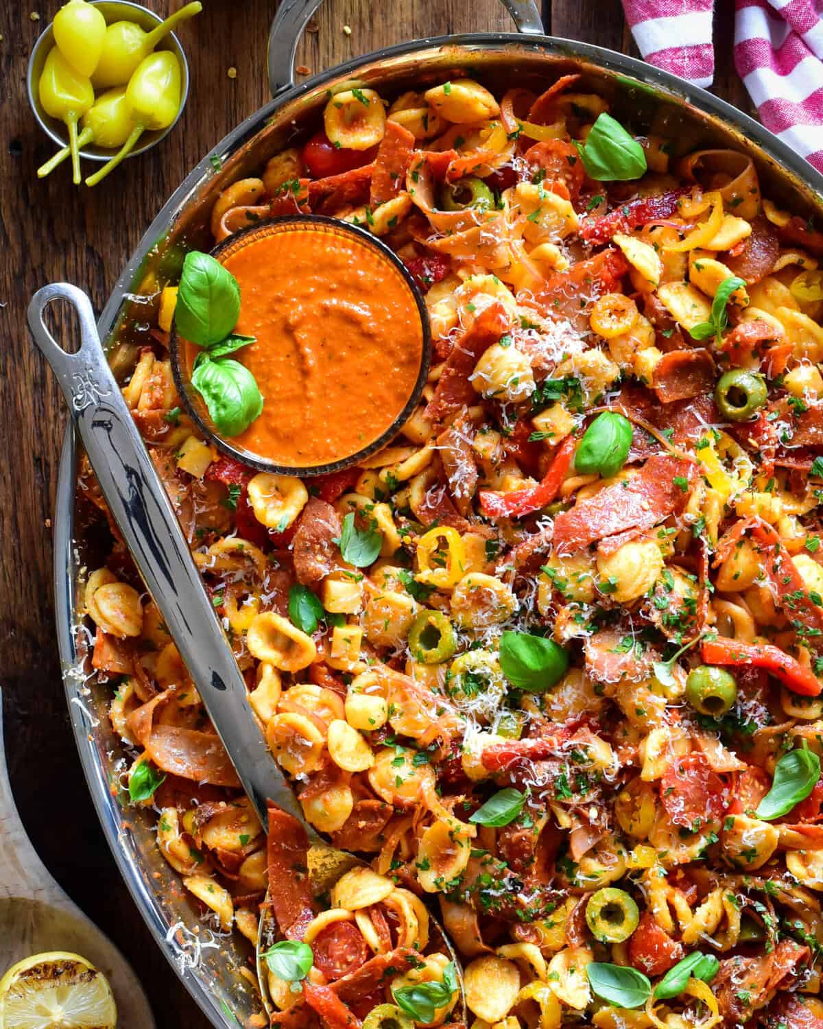 A chopped Italian romesco pasta salad with crispy spicy deli meats in a platter with extra sauce.