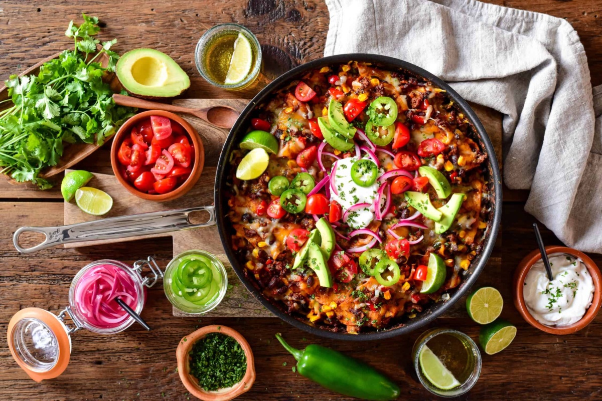 Fresh Mexican-style skillet with black beans, cherry tomatoes, avocado slices, red onions, and jalapeños garnished with lime wedges. Perfect for a flavourful, healthy meal or snack.