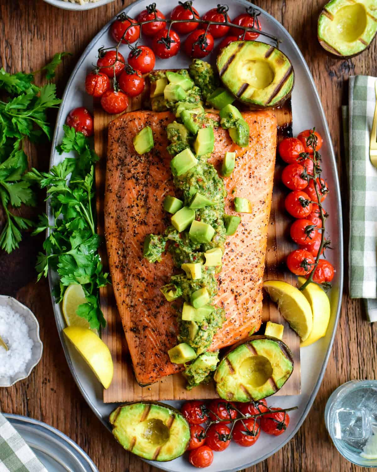 Cedar plank salmon topped with a smoky, chunky grilled avocado chimichurri salsa and charred tomatoes on the vine.
