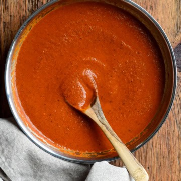A skillet of homemade fire-roasted enchilada sauce with a wooden spoon.