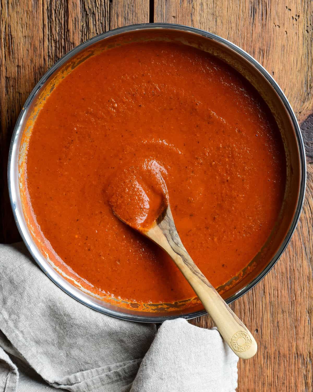 A skillet of homemade fire-roasted enchilada sauce with a wooden spoon.