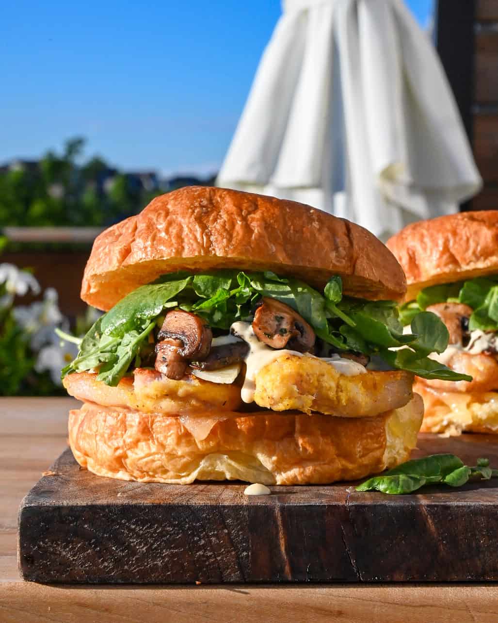 A Steakhouse Peameal Bacon Sandwich with Mushrooms, garlic aioli and greens outdoors with a blue sky.