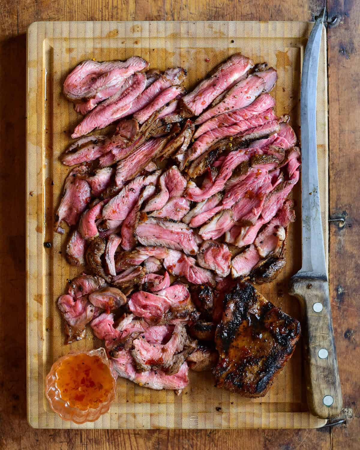 Medium rare, sliced Australian, grilled boneless leg of lamb on a cutting board with a large knife.