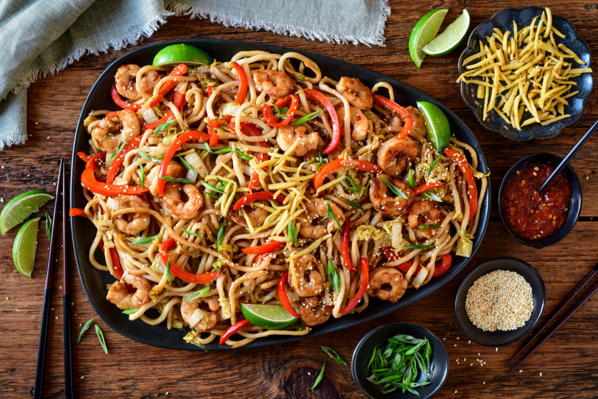 A platter of Sticky Soy Argentinian Shrimp & Fried Ginger Udon. Served with extra fried ginger, limes, sesame seeds and green onions.