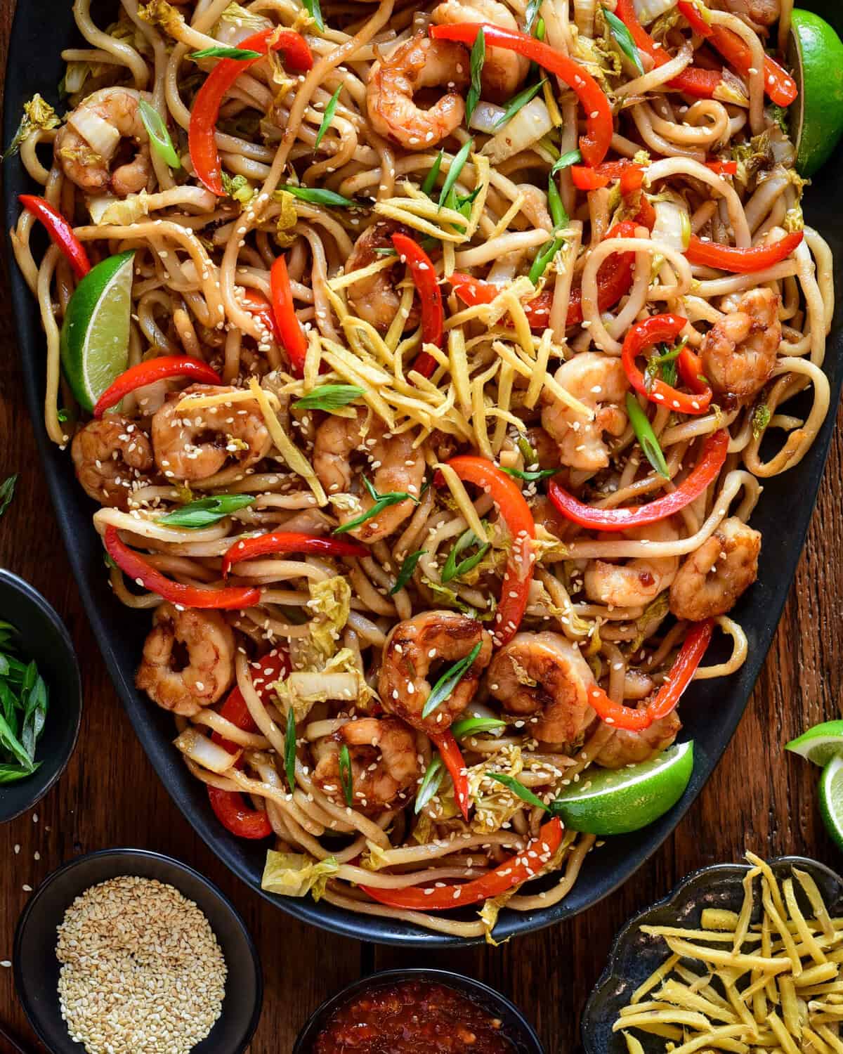 A platter of Sticky Soy Argentinian Shrimp & Fried Ginger Udon. Served with extra fried ginger, limes, sesame seeds and green onions.