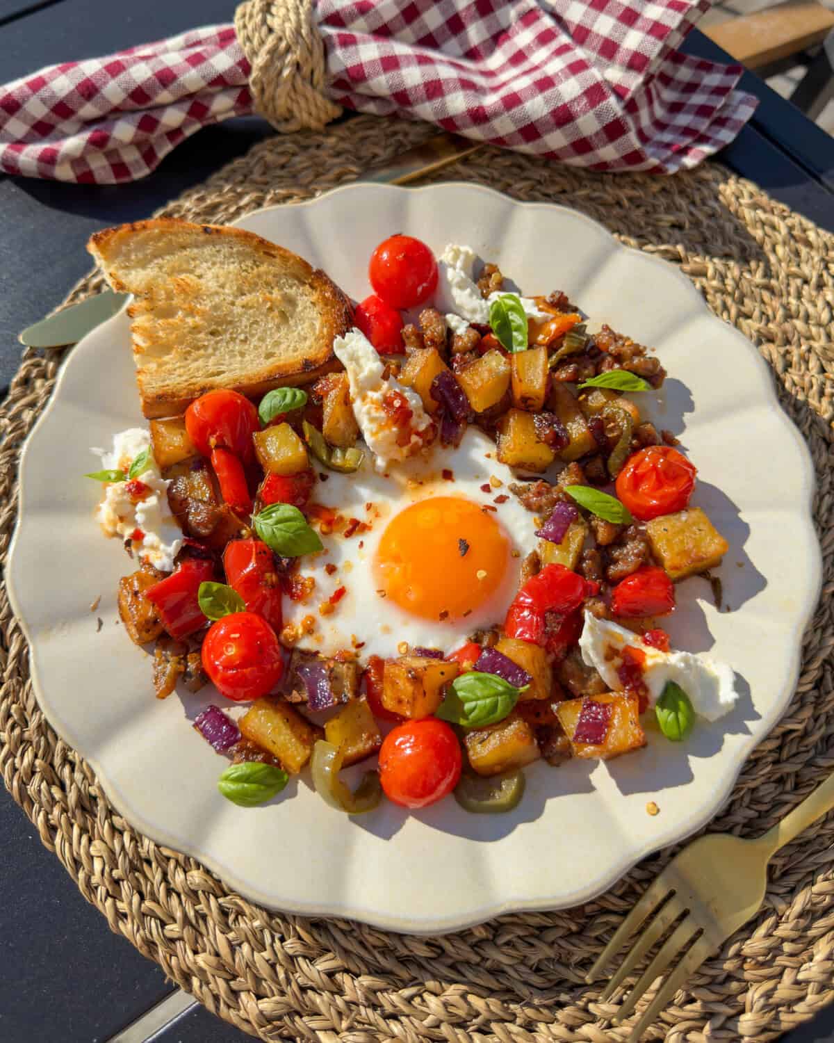 A breakfast hash served with a sunnyside-up egg in the centre, torn burrata, basil and a piece of toast.