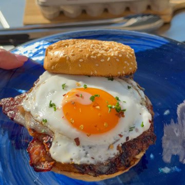 A sausage and sunny-side egg breakfast smash burger on a blue glass plate.
