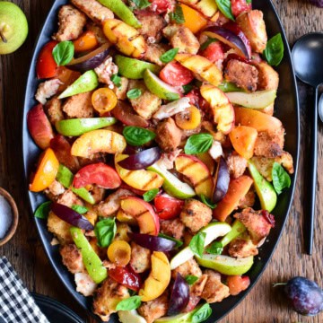 Colorful late summer stone fruit panzanella salad with fresh basil on a black platter, featuring peaches, plums, and tomatoes, perfect for seasonal dining.