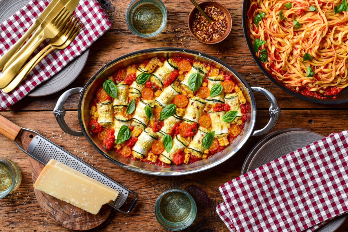 Baked zucchini involtini filled with ricotta cheese and corn, garnished with basil, served in a baking dish on a rustic wooden table.