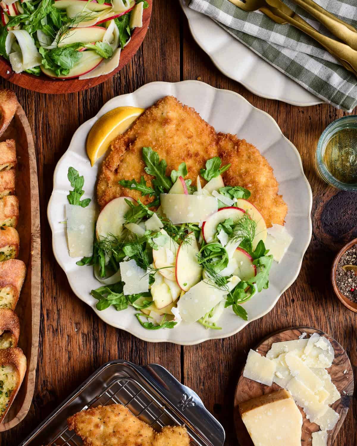 Golden crispy chicken Milanese served with fresh apple fennel salad and lemon wedge on a white plate.