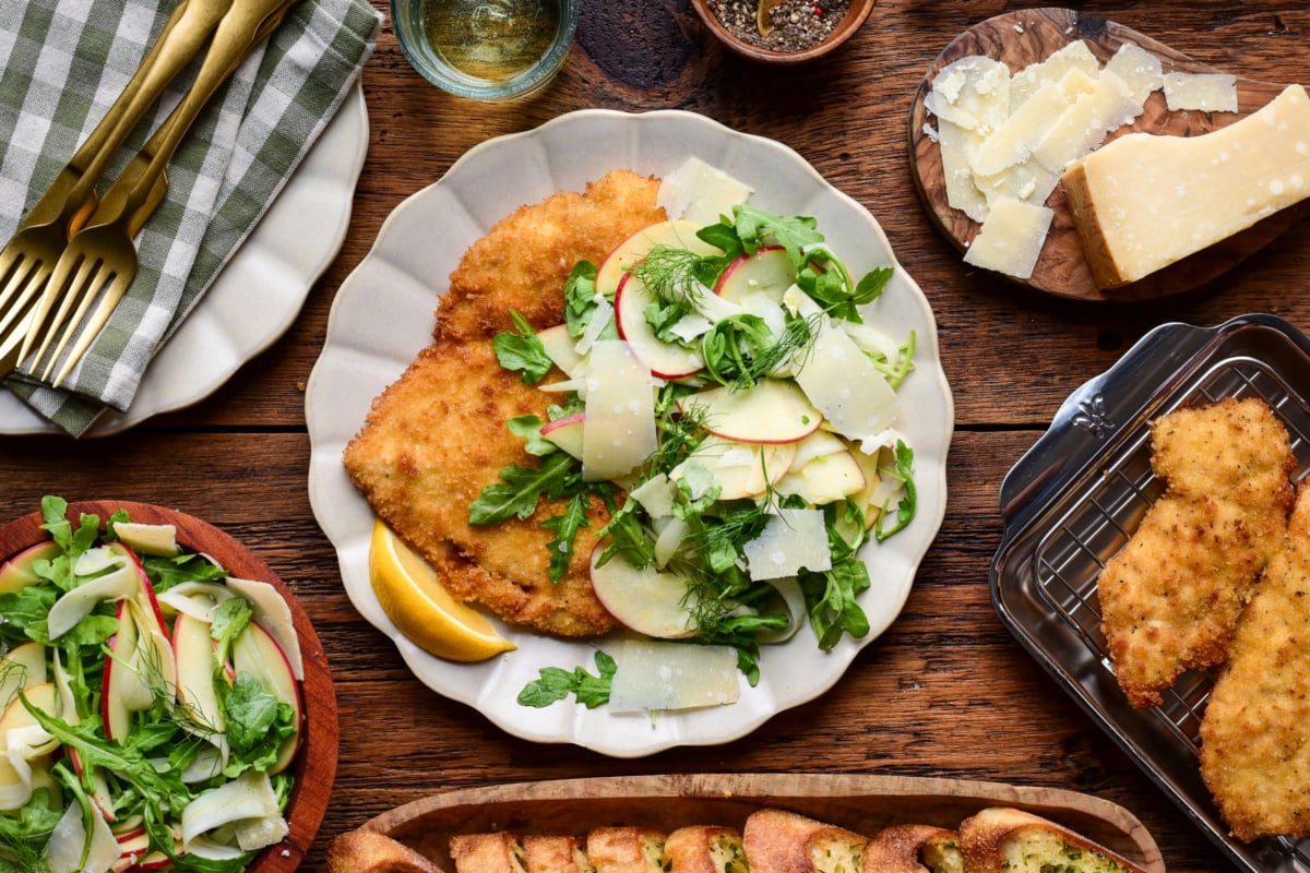 Golden crispy chicken Milanese served with fresh apple fennel salad and lemon wedge on a white plate.