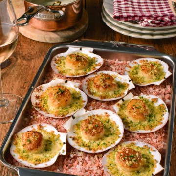 Baked scallops in shells with a breadcrumb topping, served on a baking tray with pink Himalayan salt, perfect for seafood lovers.
