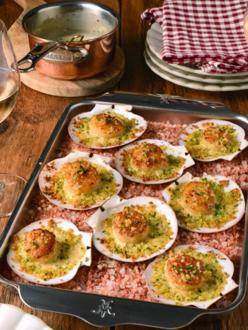 Baked scallops in shells with a breadcrumb topping, served on a baking tray with pink Himalayan salt, perfect for seafood lovers.