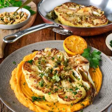 Delicious golden cauliflower steaks served with whipped sweet potatoes and garnished with herbs, perfect for a healthy vegan meal.