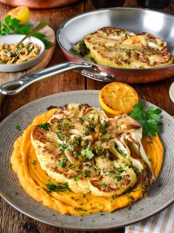 Delicious golden cauliflower steaks served with whipped sweet potatoes and garnished with herbs, perfect for a healthy vegan meal.