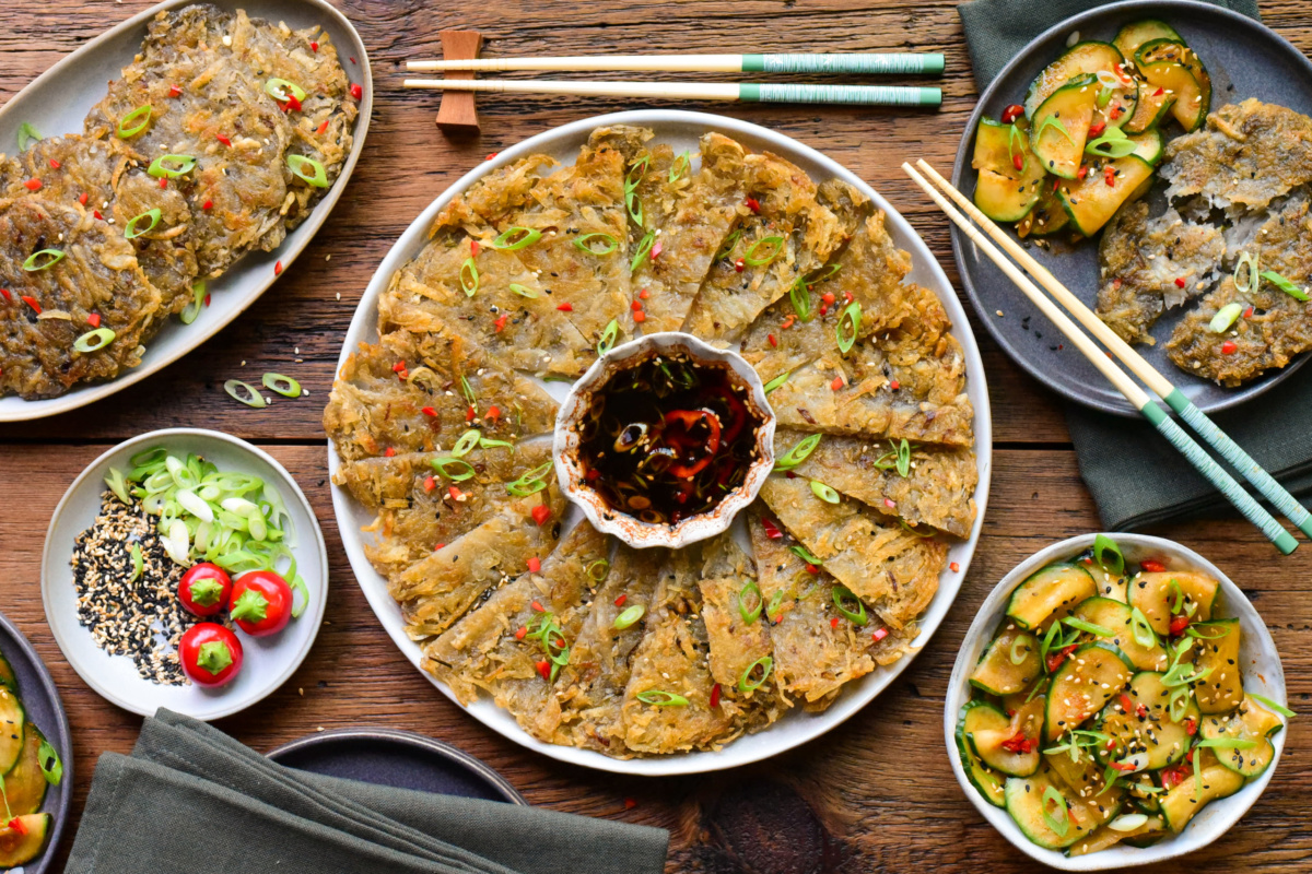 Korean Gamja-Jeon potato pancakes served with spicy cucumber salad, garnished with green onions and sesame seeds, on a wooden table.