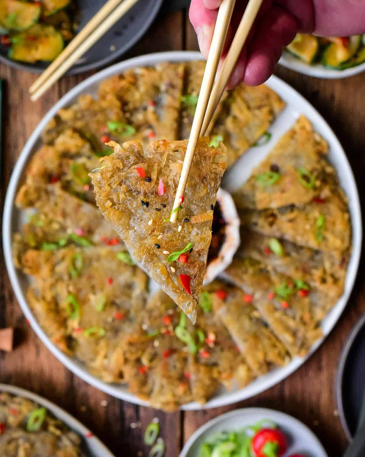 Close-up of crispy Korean Gamja-Jeon potato pancakes garnished with green onions and red pepper flakes, served on a white plate with dipping sauce.