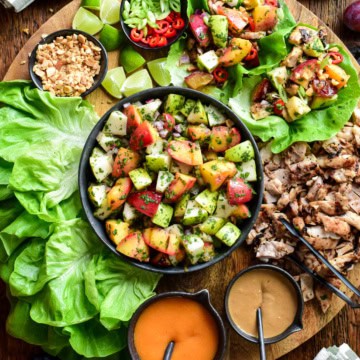 Colourful late-summer fruit and grilled chicken lettuce wraps with fresh fruits and sauces on a wooden platter.