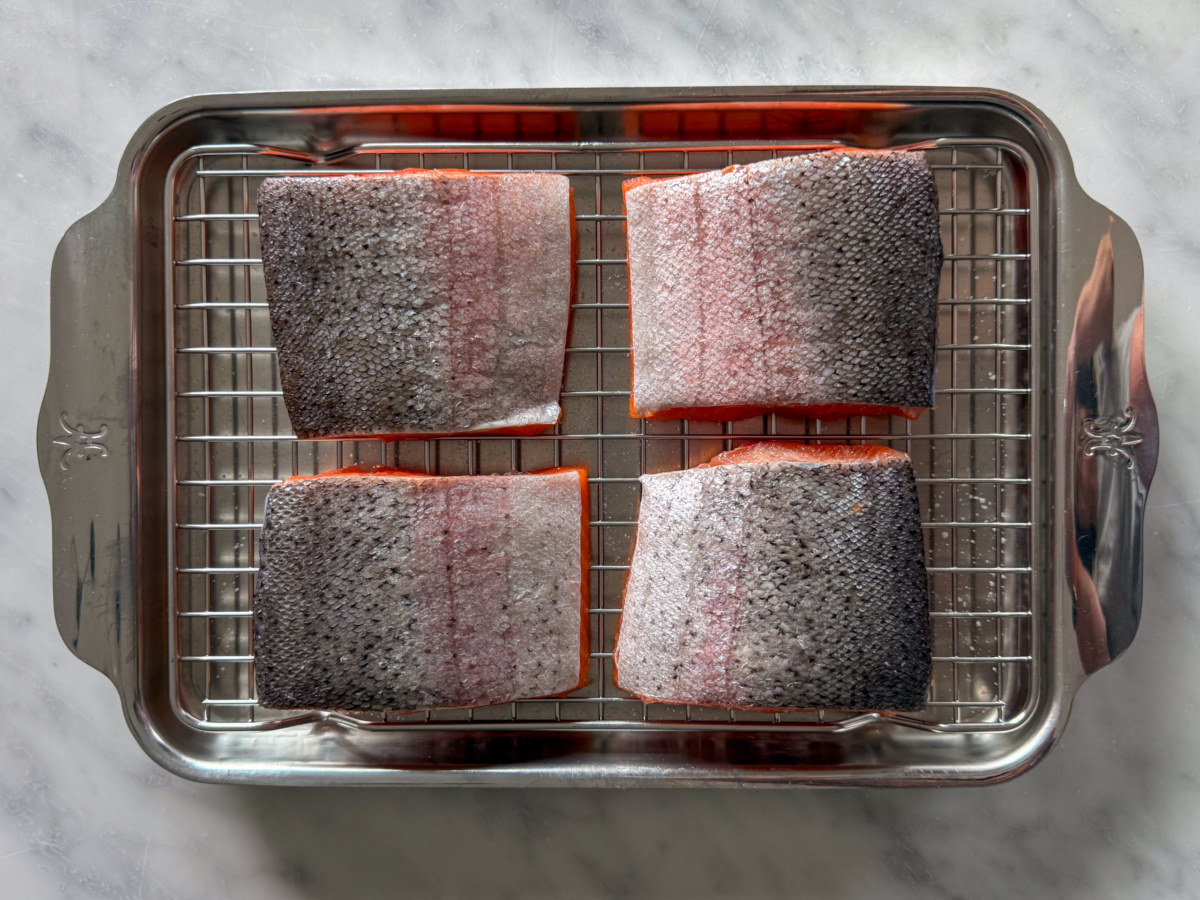 Four portions of steelhead trout, skin side up on a rack in a tray.