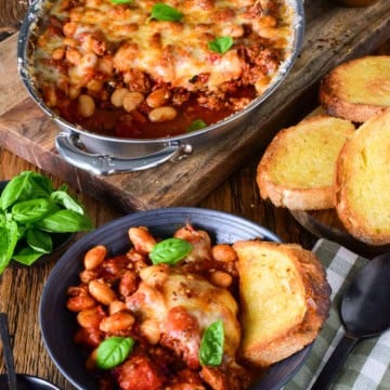 Delicious pizza beans skillet with spicy sausage, melted cheese, and fresh basil, served with toasted garlic bread on a rustic wooden table.