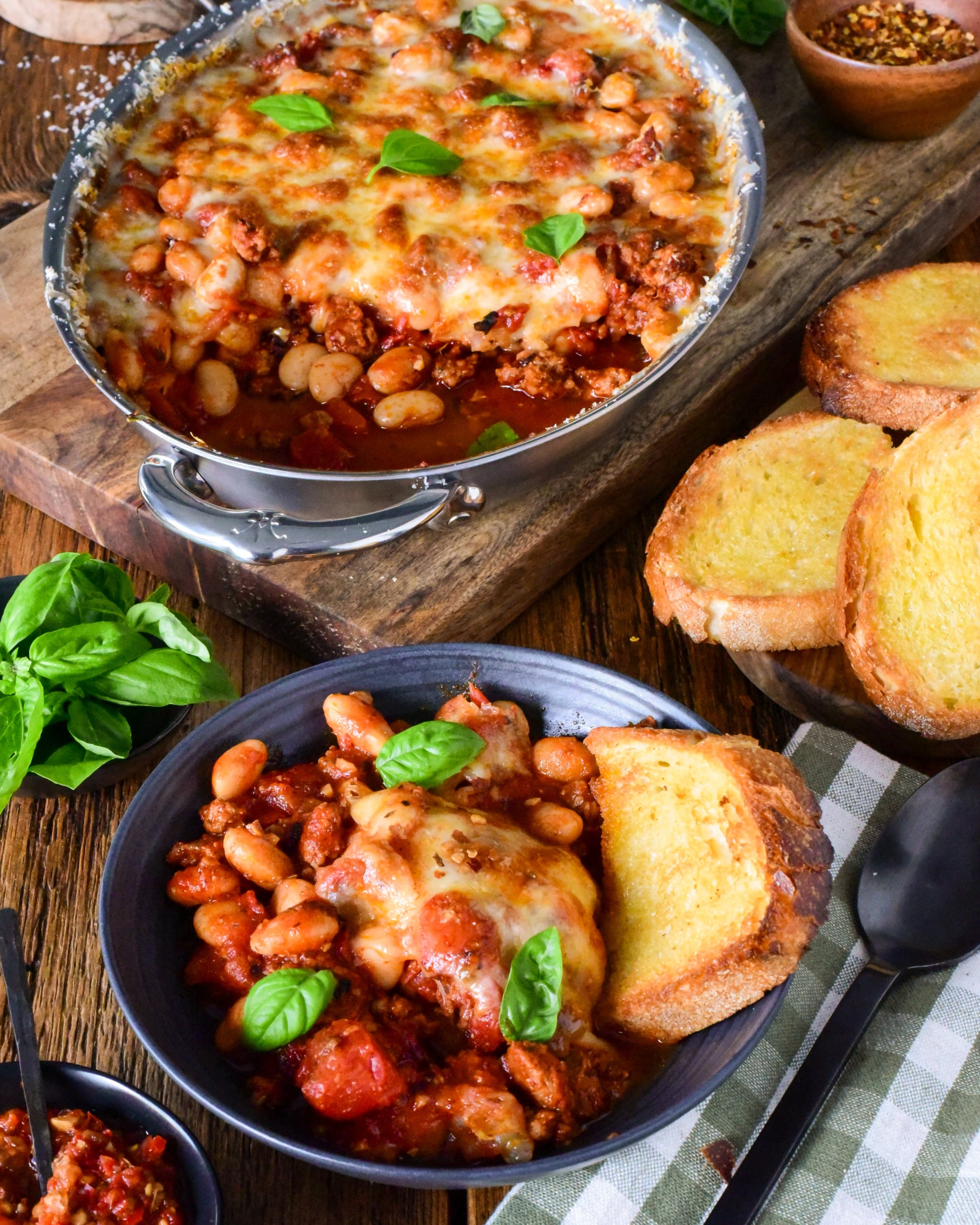 Delicious pizza beans skillet with spicy sausage, melted cheese, and fresh basil, served with toasted garlic bread on a rustic wooden table.